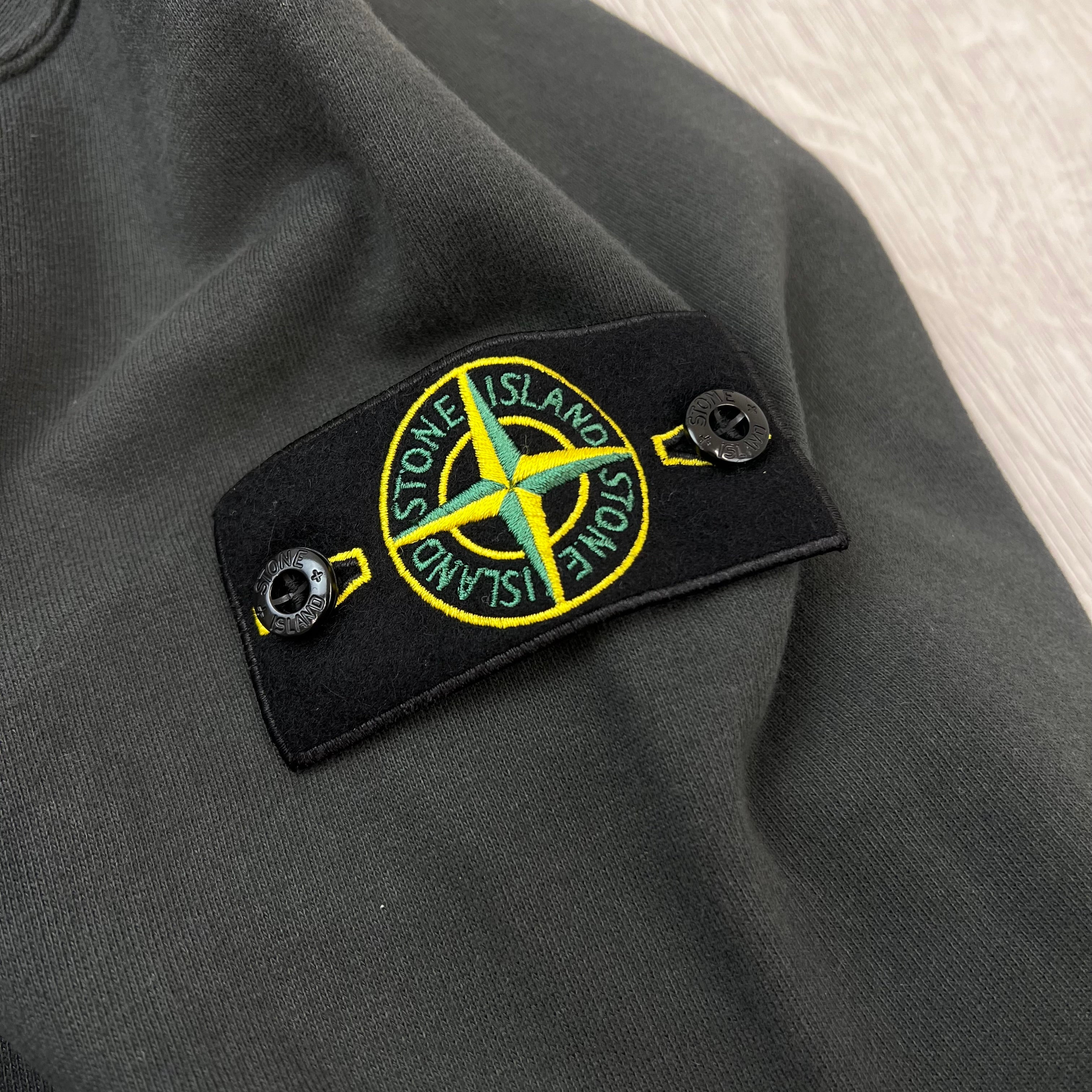 A close up view of the compass badge on a Stone Island Crewneck Brushed Cotton Sweatshirt in Lead Grey.