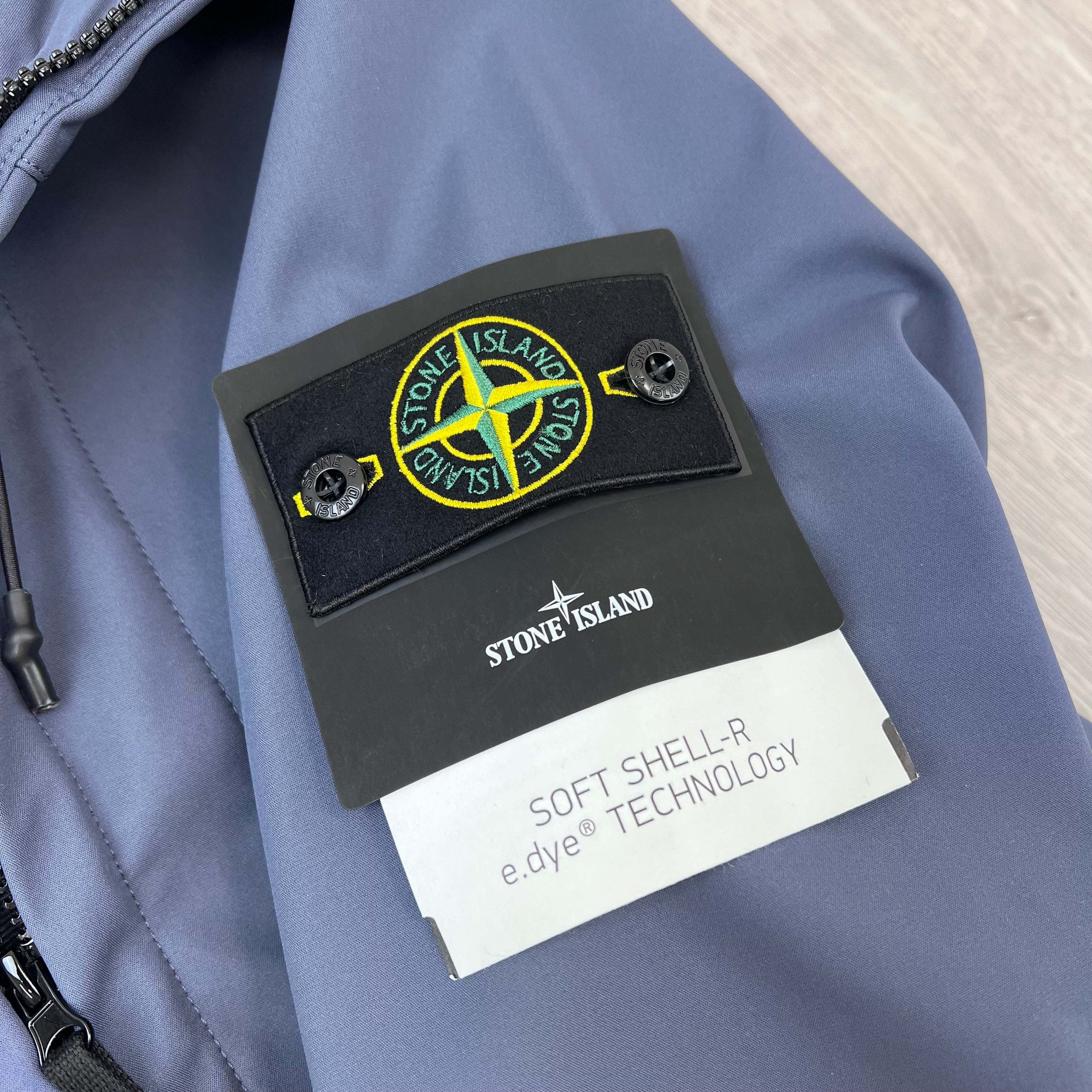 A close up view of the badge logo on the sleeve of a Stone Island Soft Shell-R_e.dye® Jacket in Slate Blue.