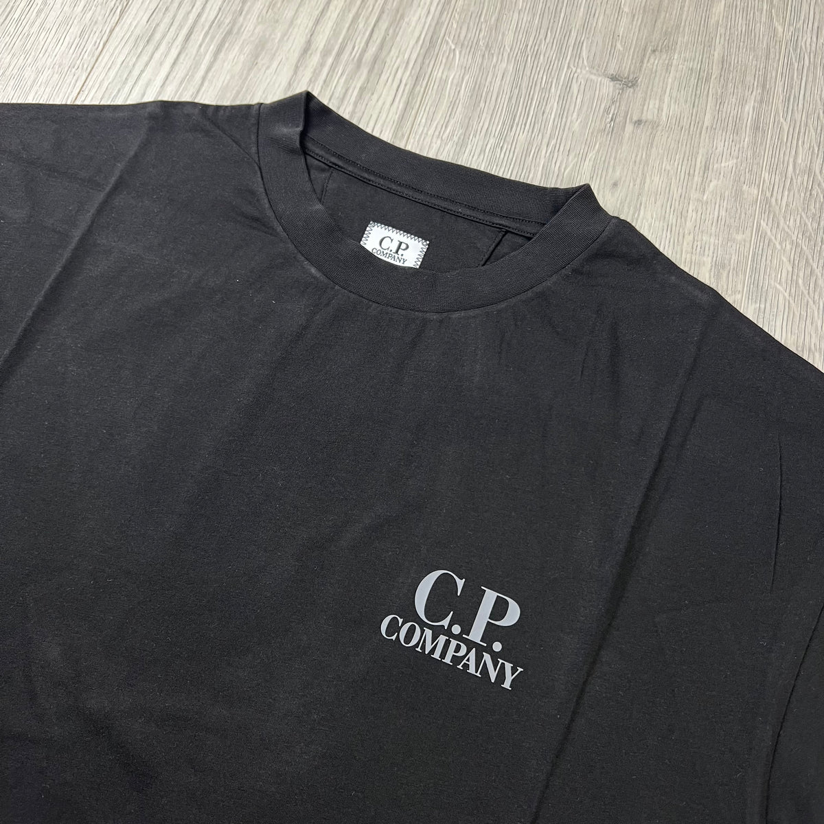 Close up view of the crewneck collar on a CP Company 30/1 Logo T-Shirt in Black. 