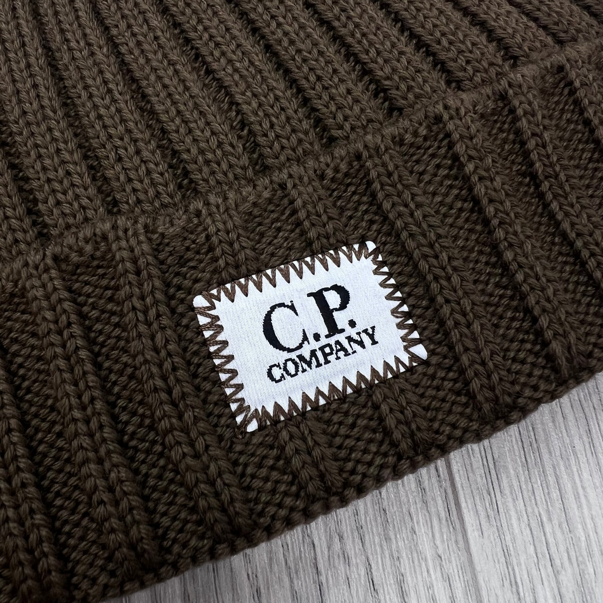Close view of the stamp logo label on a CP Company Merino Wool Patch Beanie in Ermine.