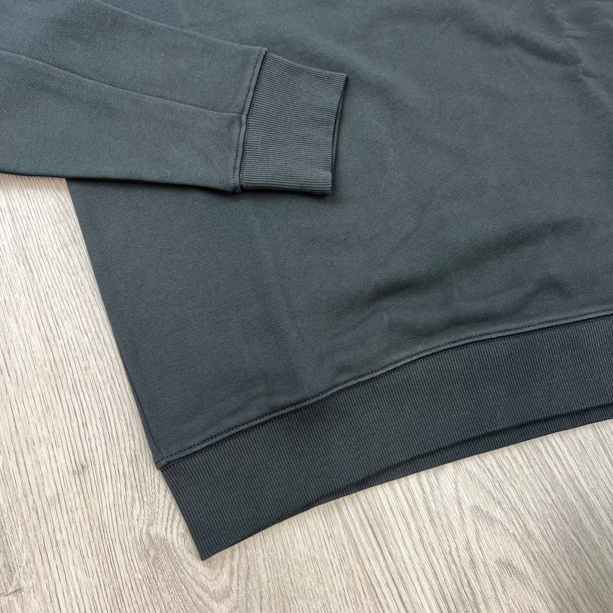 Close up view of the ribbed hem and cuffs on a CP Company Raised Fleece Sweatshirt in Raven Grey. 