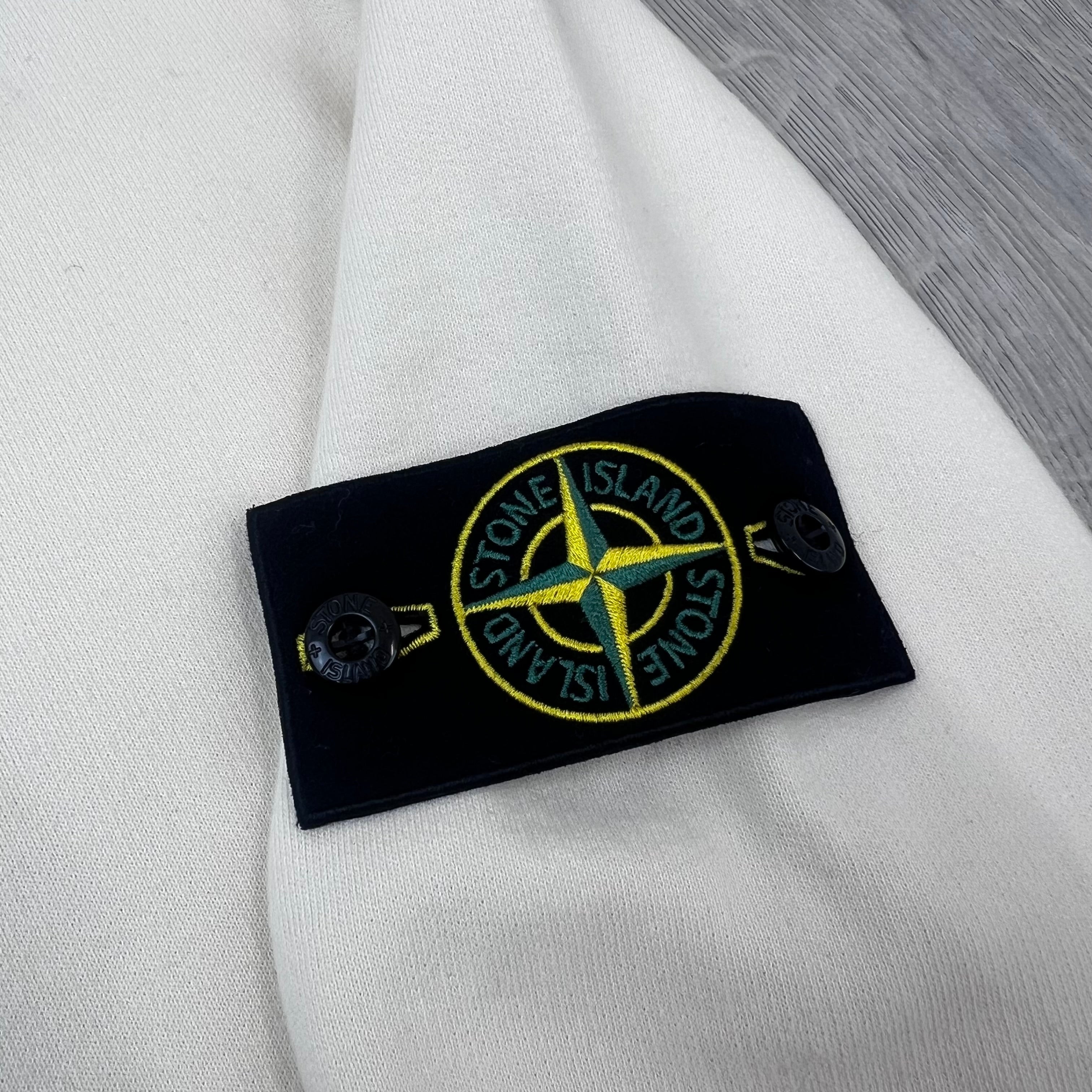 A close up view of the compass badge on a Stone Island Crewneck Brushed Cotton Sweatshirt in Ivory.