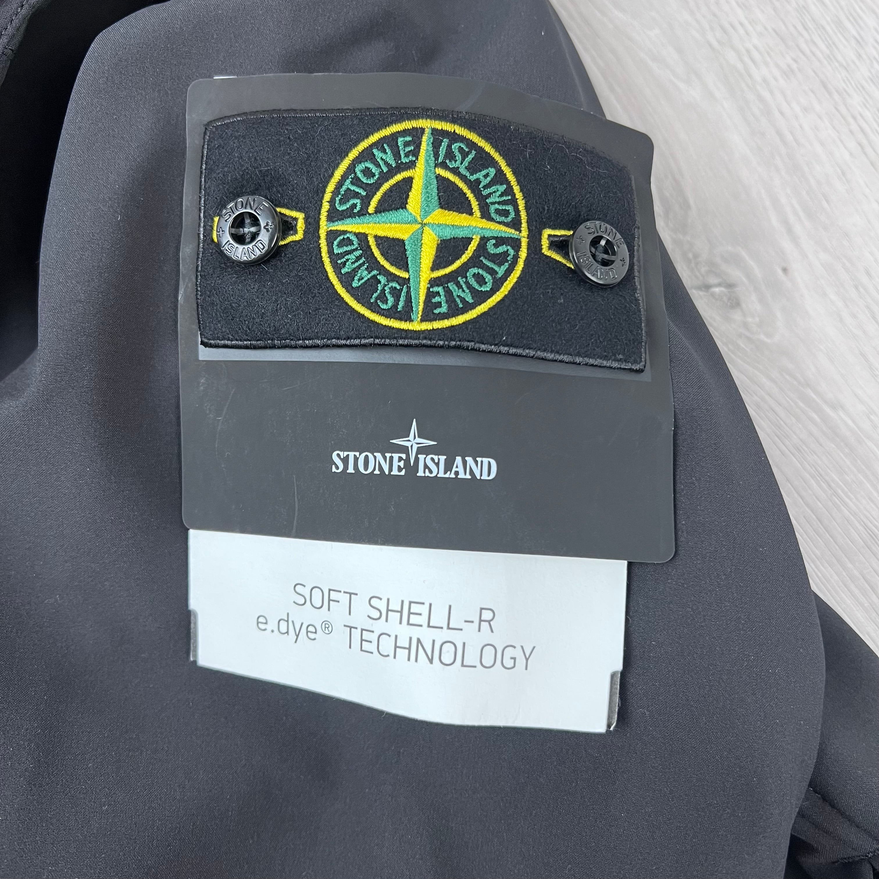 A close up view of the badge logo on the sleeve of a Stone Island Soft Shell-R_e.dye® Jacket in Black.