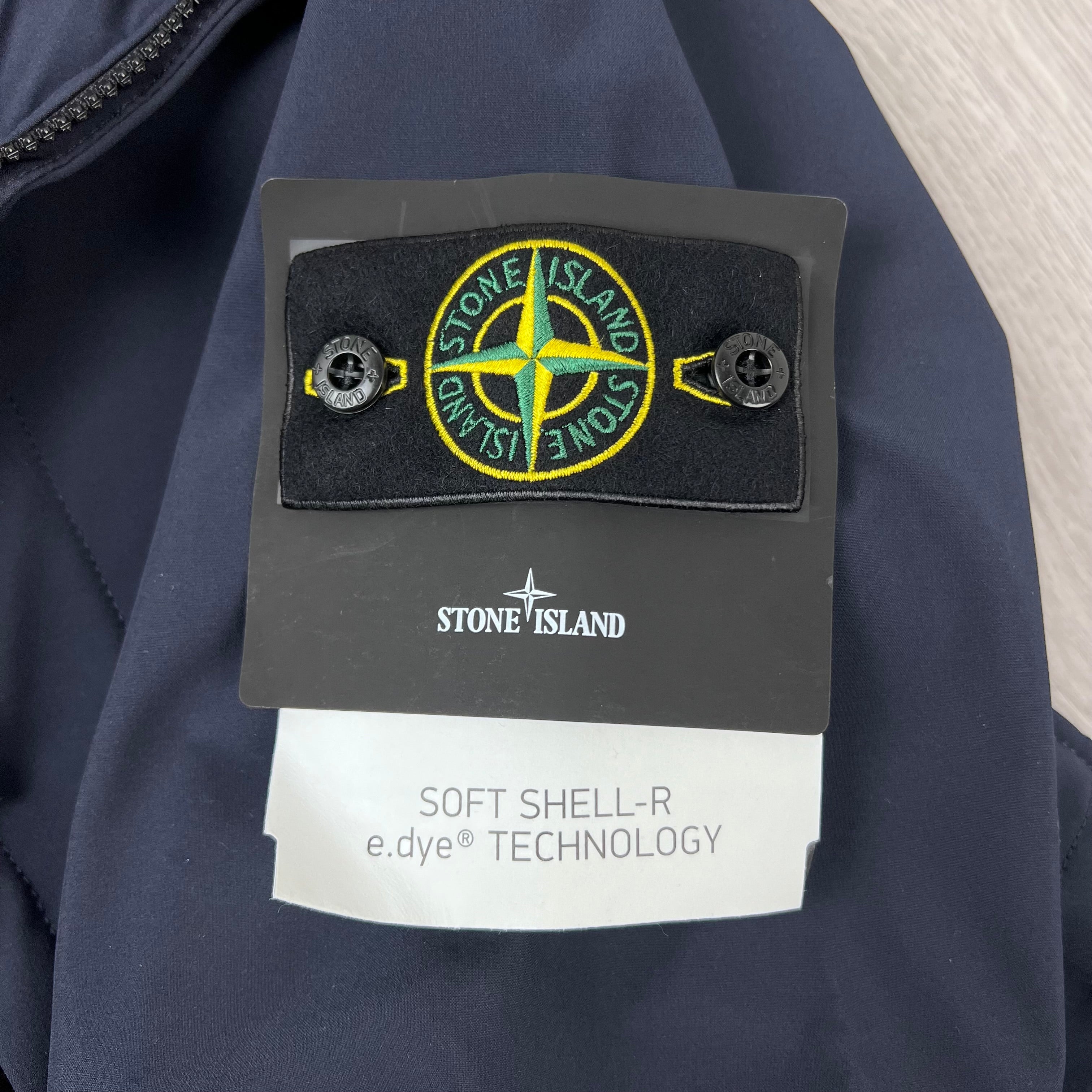 A close up view of the badge logo on the sleeve of a Stone Island Soft Shell-R_e.dye® Jacket in Navy Blue.